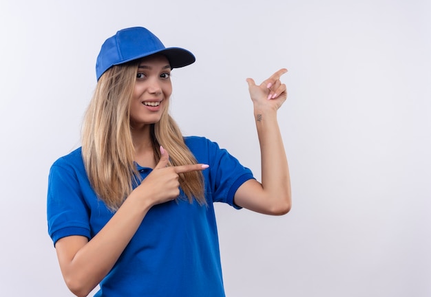 Foto gratuita la giovane ragazza sorridente di consegna che porta l'uniforme blu e punti del cappuccio al lato isolato sulla parete bianca con lo spazio della copia