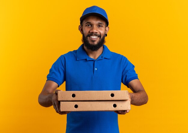 smiling young delivery man holding pizza boxes isolated on orange wall with copy space