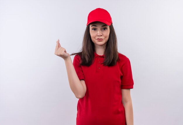赤い帽子に赤いtシャツを着ている若い配達の女性の笑顔は、孤立した白い壁にヒントを求める
