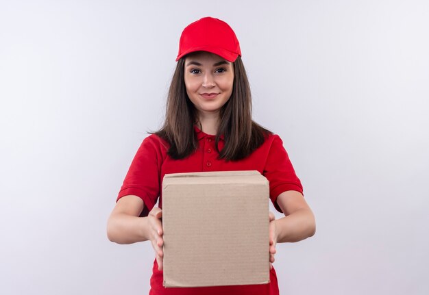 Улыбающаяся молодая женщина-доставщик в красной футболке в красной кепке держит коробку на изолированной белой стене