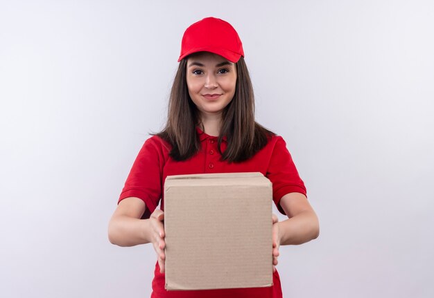 Smiling young delivery woman wearing red t-shirt in red cap holding a box on isolated white wall