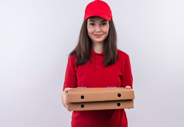 Улыбающаяся молодая женщина-доставщик в красной футболке в красной кепке держит коробку для пиццы на изолированной белой стене