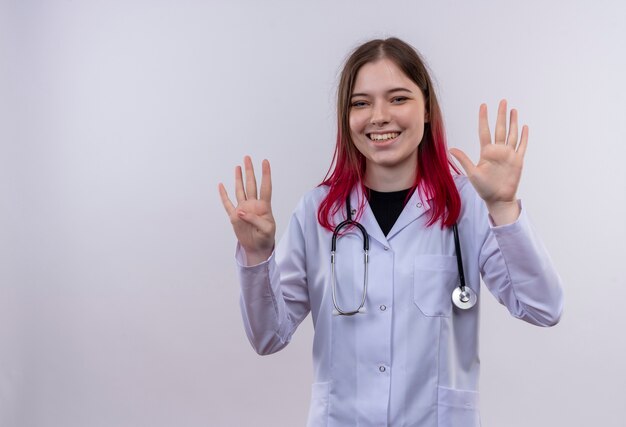 コピースペースと孤立した白い背景に異なる番号を示す聴診器医療ローブを着て笑顔の若い医者の女の子