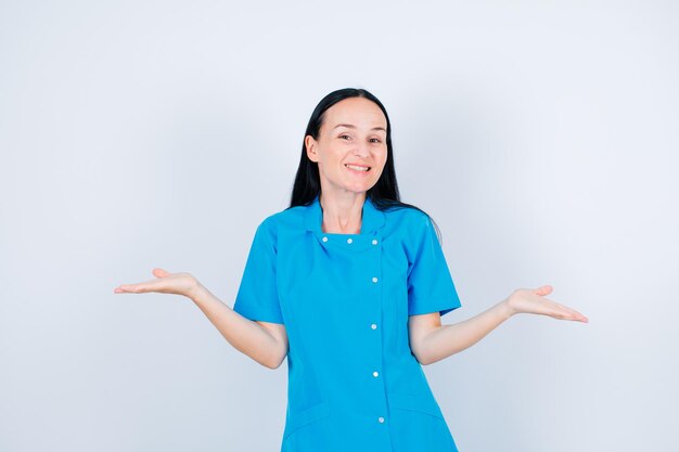Smiling young doctor is looking at camera by opening wide her arms on white background