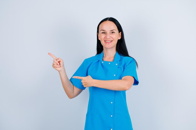 Smiling young doctor is pointing left with forefingers on white background