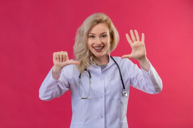 Улыбающийся молодой врач со стетоскопом в медицинском халате, показывающий разные жесты на красном фоне