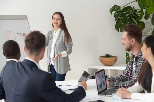 Smiling young employee giving presentation working with flipchart in meeting room