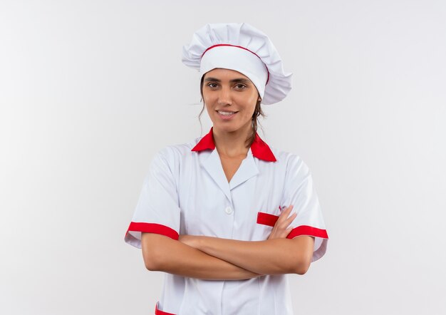 Smiling young female cook wearing chef uniform crossing hands with copy space