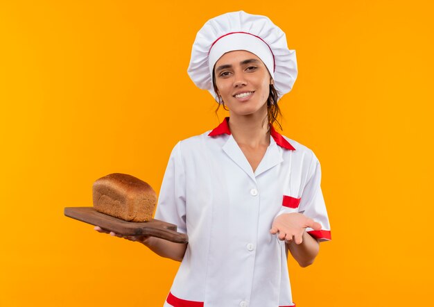 コピースペースとまな板にパンを保持しているシェフの制服を着て笑顔の若い女性料理人