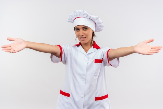 Sorridente giovane femmina cuoco indossando lo chef uniforme tendendo le mani alla telecamera