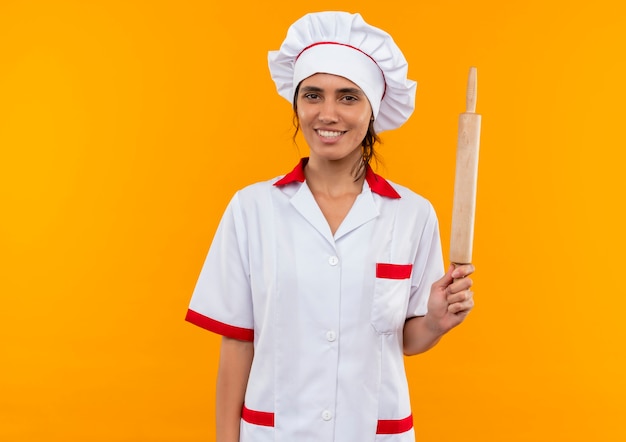 Smiling young female cook wearing chef uniform holding rolling pin with copy space