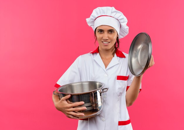 Smiling young female cook wearing chef uniform holding saucepan and lid with copy space