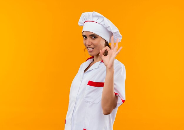 Smiling young female cook wearing chef uniform showing okey gesture  with copy space