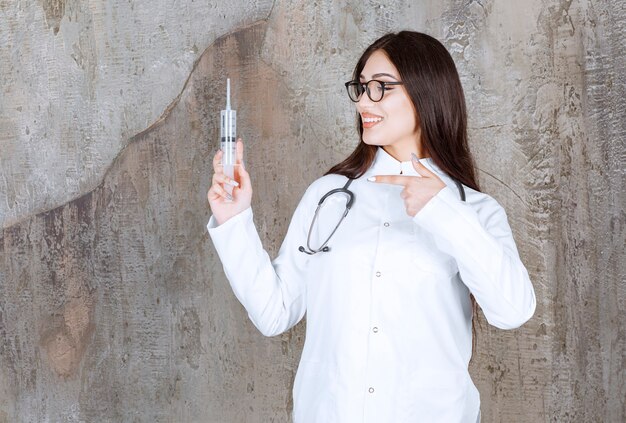 Smiling young female doctor holding injection and pointing finger on it