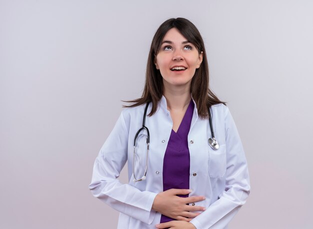 聴診器と医療ローブで笑顔の若い女性医師は、コピースペースと孤立した白い背景に両手で腹を保持します。