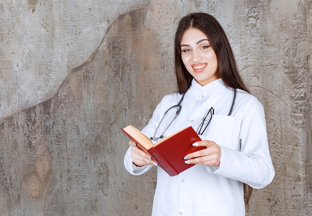 회색 벽에 책을 읽고 웃는 젊은 여성 의사