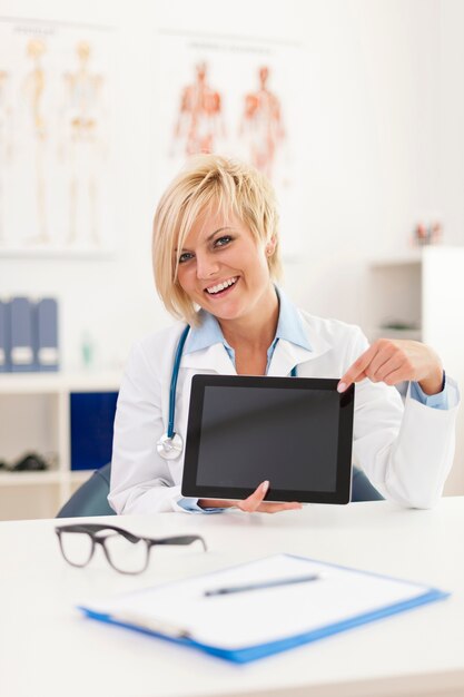Smiling young female doctor showing on screen of digital tablet