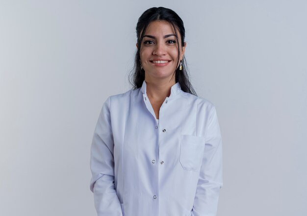 Smiling young female doctor wearing medical robe looking isolated