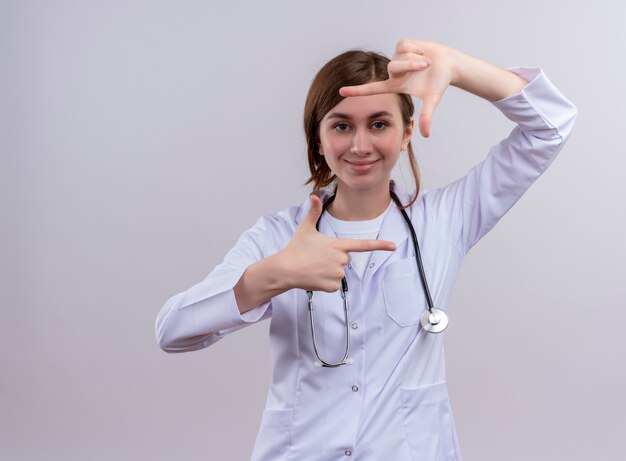 孤立した白い壁にフレームジェスチャーを行う医療ローブと聴診器を身に着けている若い女性医師