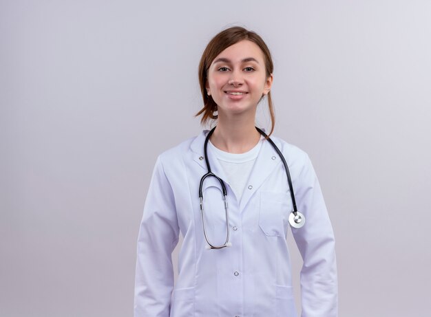 Улыбающаяся молодая женщина-врач в медицинском халате и стетоскопе на изолированной белой стене с копией пространства