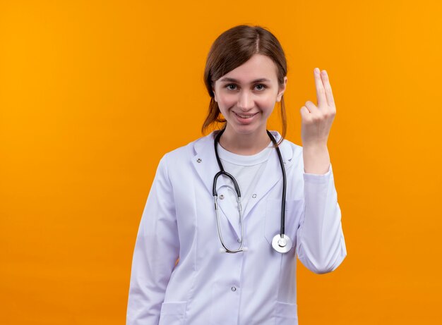 コピースペースと孤立したオレンジ色の壁に2つを示す医療ローブと聴診器を身に着けている若い女性医師の笑顔