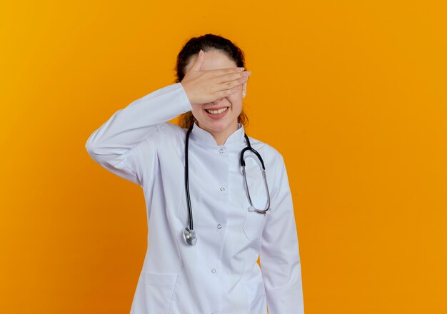 分離された手の目で覆われた眼鏡と医療ローブと聴診器を身に着けている若い女性医師の笑顔