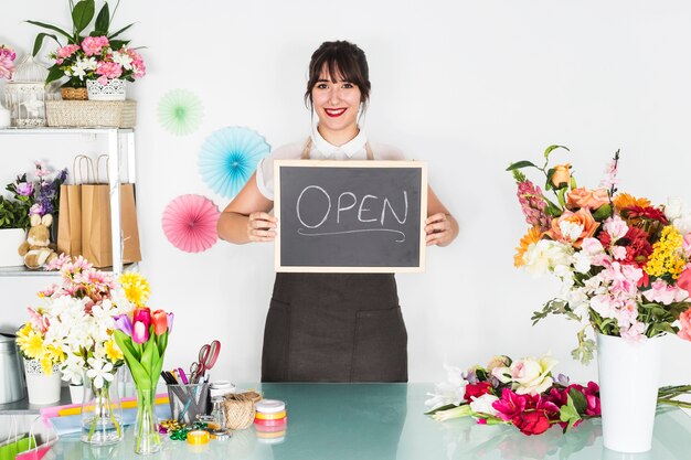 Smiling young female florist showing slate with open word