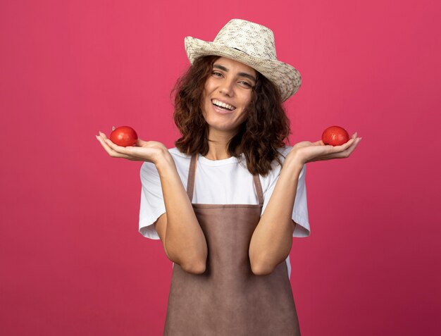 トマトを保持している園芸帽子を身に着けている制服を着た若い女性の庭師の笑顔