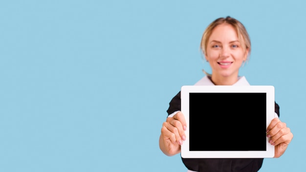 Улыбающийся молодой женский уборщик держит цифровой планшет на синем фоне