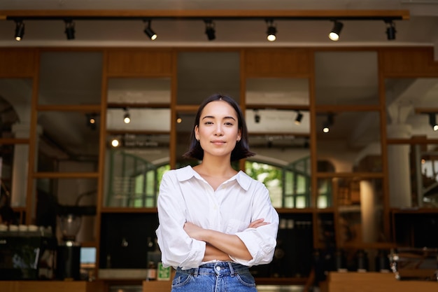 Free photo smiling young female manager cafe owner cross arms on chest looking confident standing in front of r