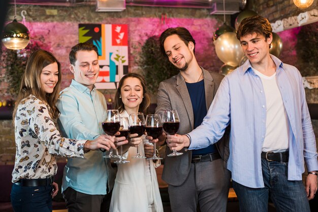 Улыбающиеся молодые друзья наслаждаются вечеринкой поджаривания вина в клубе