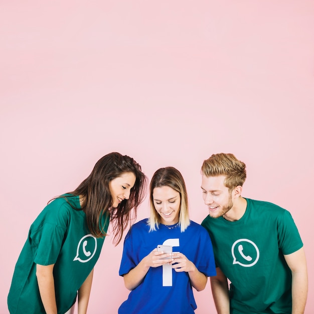 Smiling young friends looking at smartphone against pink background