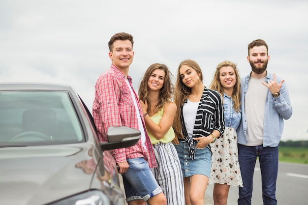 Foto gratuita sorridenti giovani amici in piedi vicino l'auto parcheggiata