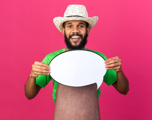 Free photo smiling young gardener afro-american guy wearing gardening hat holding speech bubble