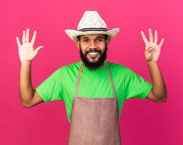 異なる数を示すガーデニングの帽子をかぶっている若い庭師のアフリカ系アメリカ人の男を笑顔
