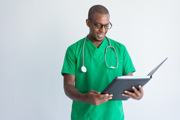 Smiling young general practitioner reading documents in folder.