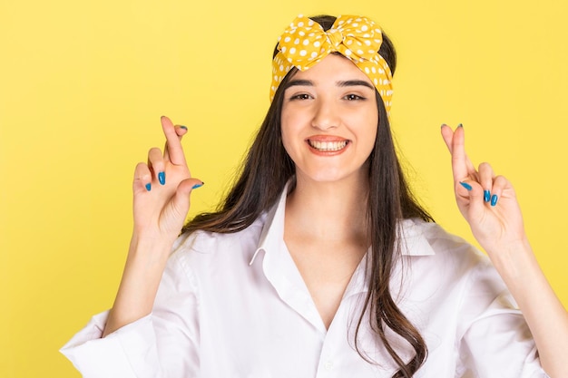 Free photo smiling young girl crossed her fingers and standing on yellow background