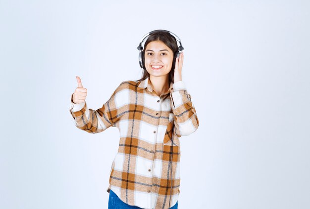 Smiling young girl in headphones listening to song and giving thumbs up. 