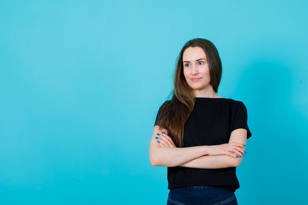 Smiling young girl is looking away by crossing arms on blue background