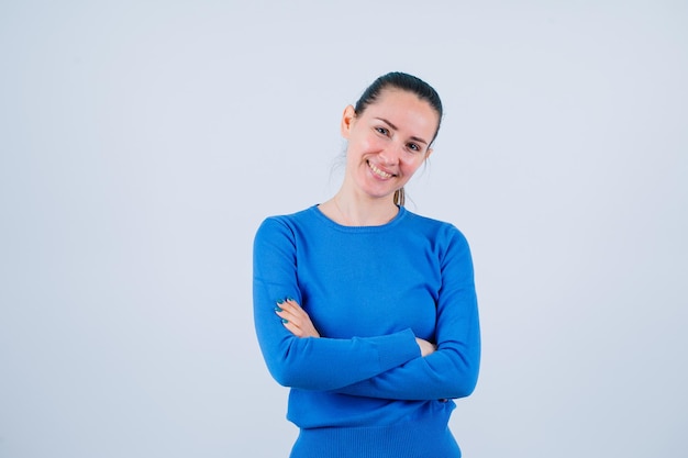 Smiling young girl is looking at camera by crossing arms on white background