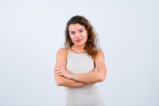 Smiling young girl is looking at camera by crossing arms on white background