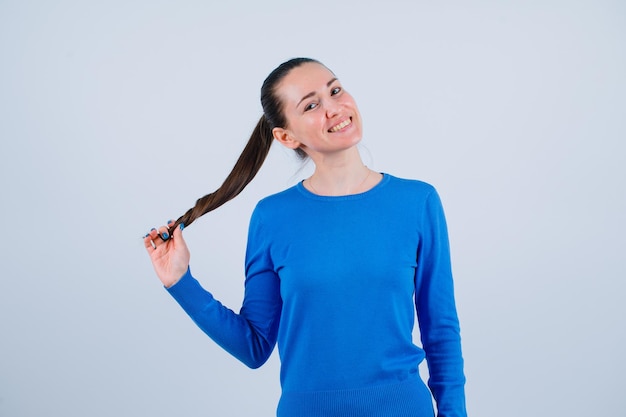 Smiling young girl is looking at camera by holding hair on white background