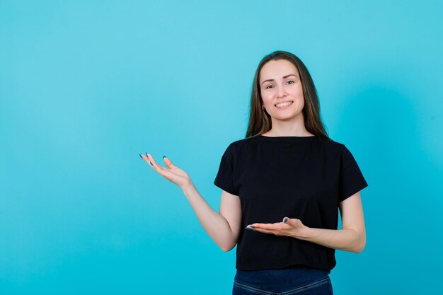 Smiling young girl is pointing left with hands on blue background