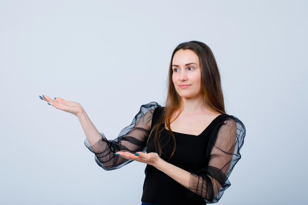 Smiling young girl is pointing left with hands on white background