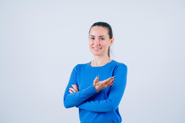 Smiling young girl is pointing right with hand by crossing arms on white background