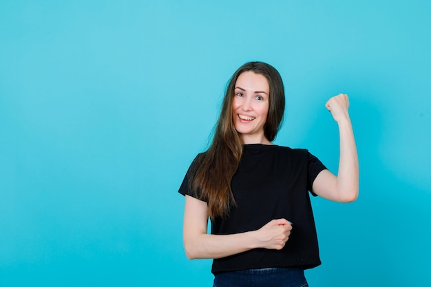 Smiling young girl is raising up her fist on blue background