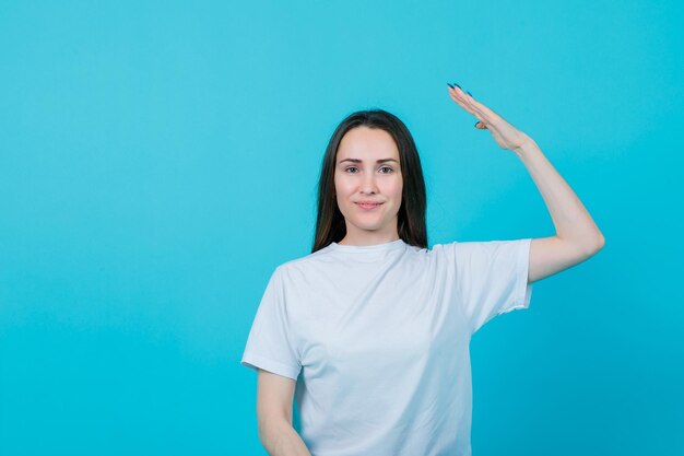 Smiling young girl is raising up her hand on blue background