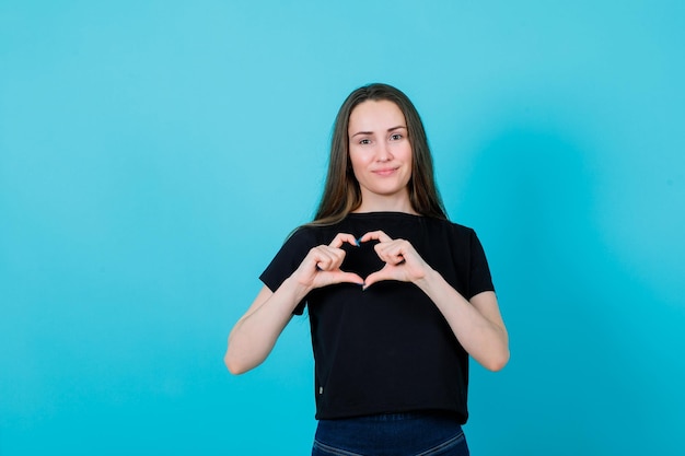 La ragazza sorridente sta mostrando il gesto del cuore con le dita su sfondo blu