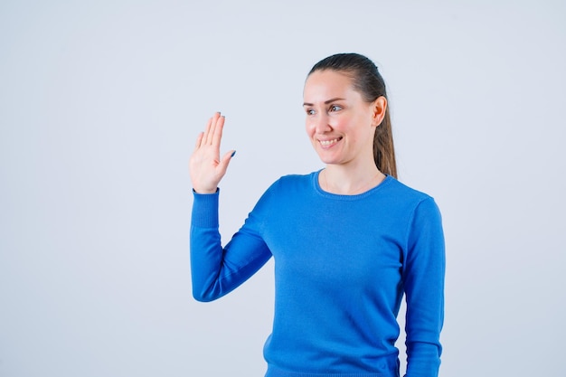 Smiling young girl is showing hi gesture on white background
