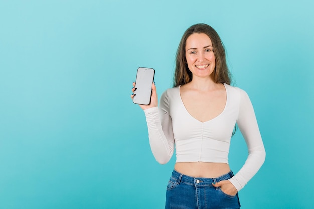 Smiling young girl is showing mockup idea by holding smartphone on blue background